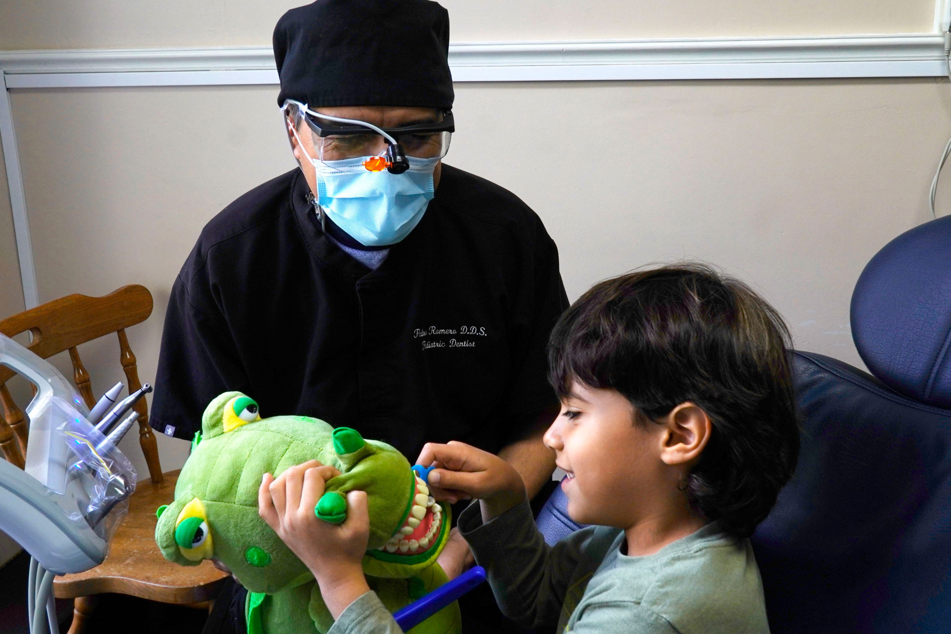 Dr. Romero showing pediatric patient how to brush teeth on stuffed toy in exam room